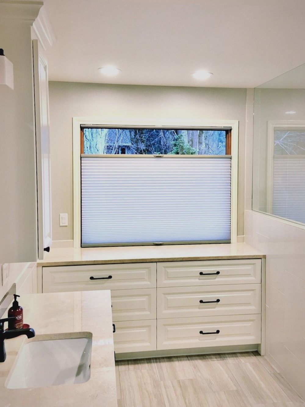 主浴室设有一个水槽柜台和带柜台的橱柜，以及一个带窗帘的玻璃窗。