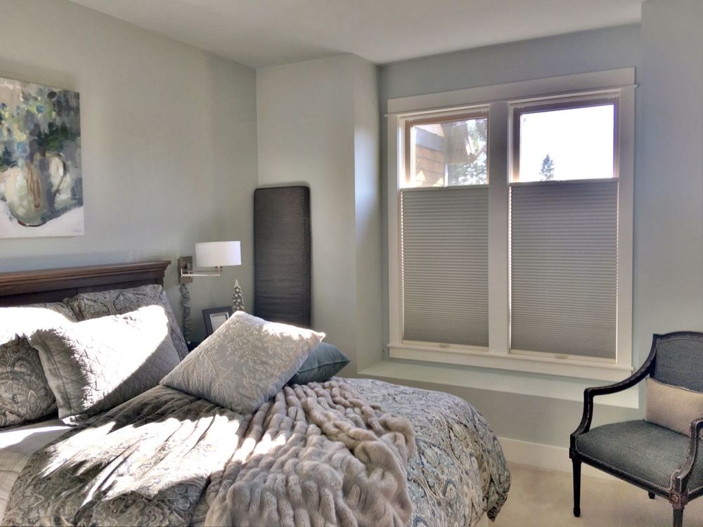 主卧室拥有一张豪华的大床，旁边有优雅的台灯。房间有灰色的墙壁，窗户上有遮阳板。
