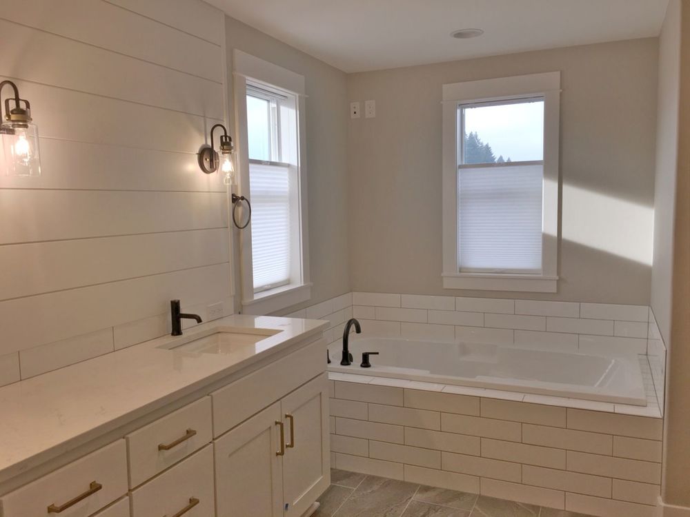 这间浴室设有一个洗涤台和一个可浸入式深泡浴缸。浴室也以灰色瓷砖地板和带遮阳板的窗户为特色。