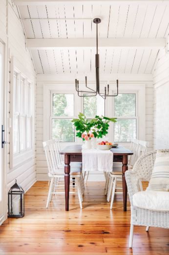 这间农舍风格的餐厅的白色餐椅与白色木门融合得很好，白色木门的饰面很迷人，与木质大教堂的船形天花板相匹配。这与硬木地板和简单的铁吊灯形成对比。