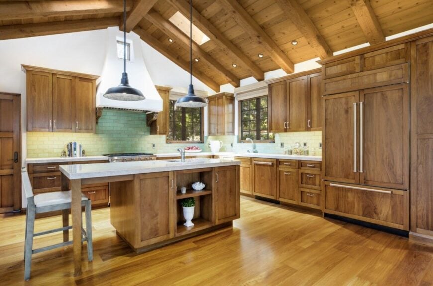 厨房设有一个带白色台面的中央岛台，还有一个单独的空间早餐吧台，由木质拱形天花板上悬挂的吊灯照明。图片来自Toptenrealestatedeals.com。