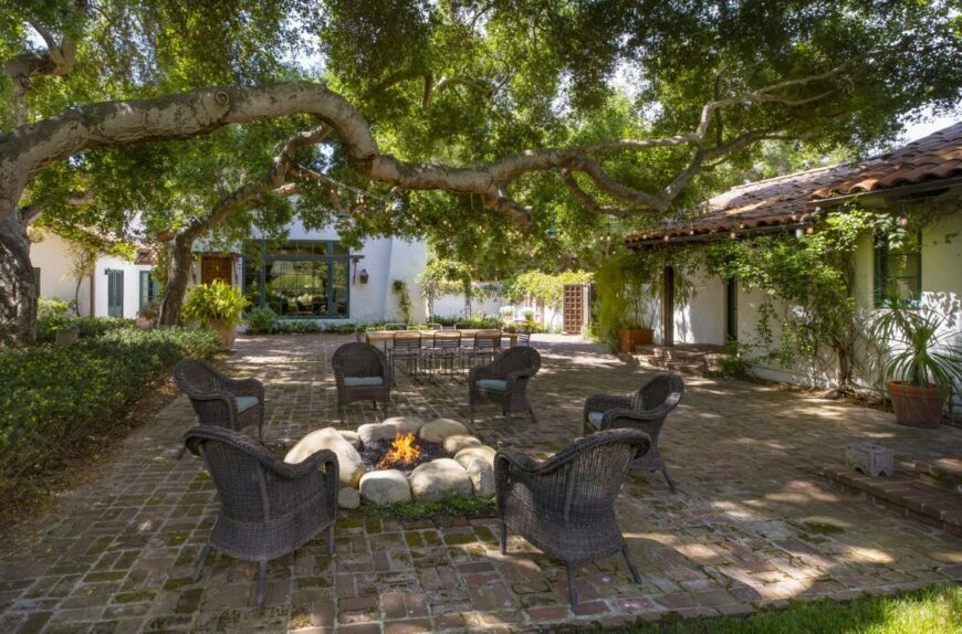 在后院，有一个带火坑的露台和一张户外矩形餐桌，周围成熟的树木为其遮荫。图片来自Toptenrealestatedeals.com。