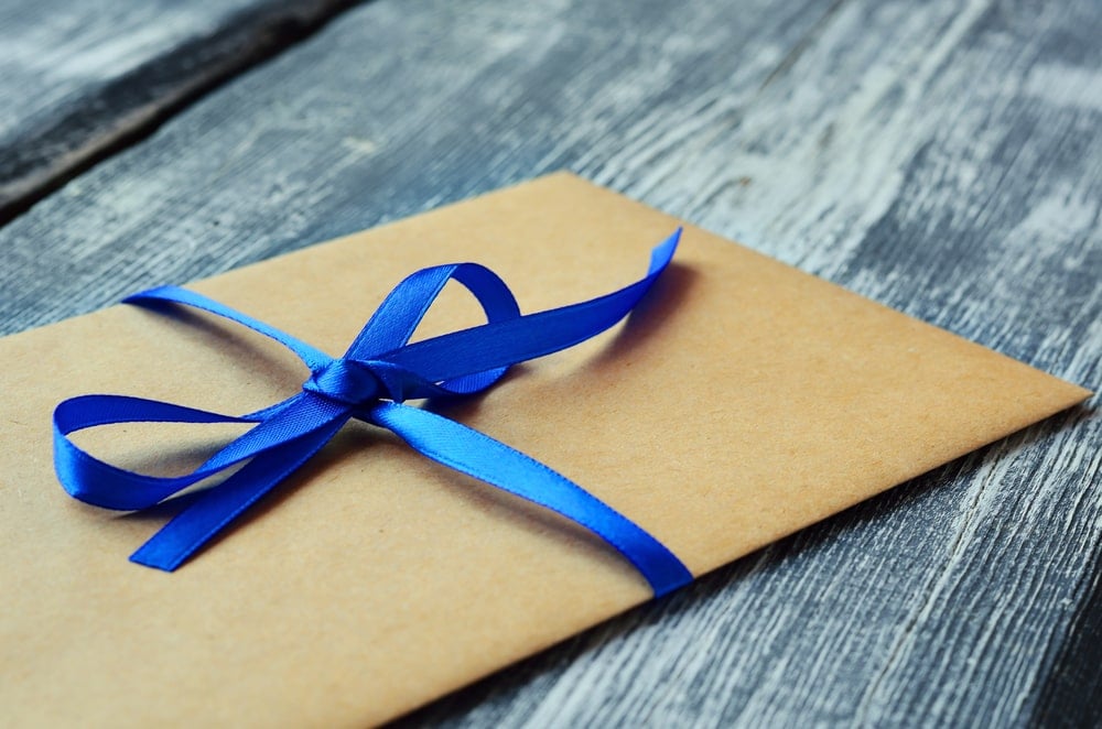 用蓝色丝带系在木质背景上的牛皮纸信封。