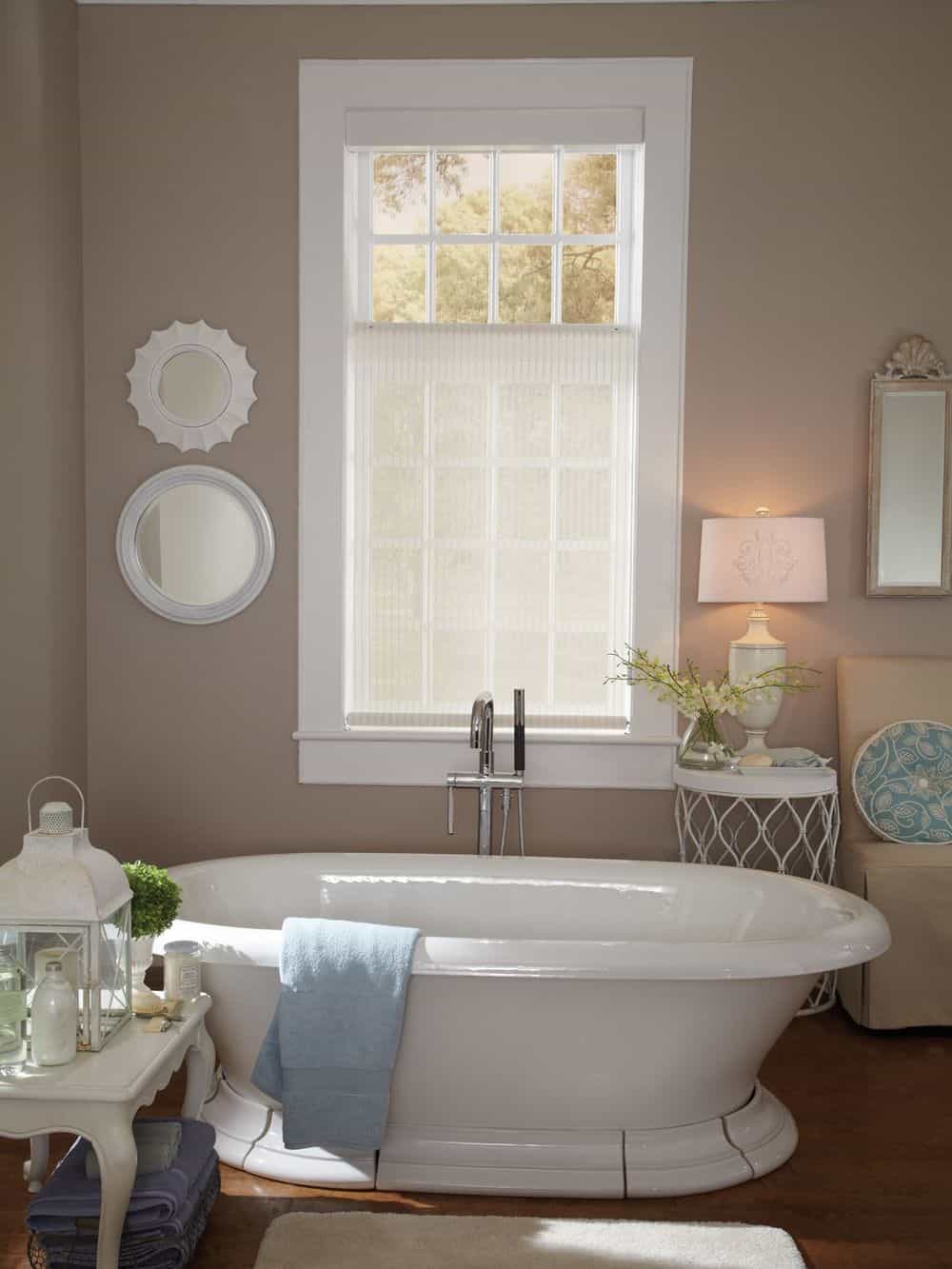 主浴室设有一个独立的浴缸和一个带有迷人台灯的边桌，以及一个带有可爱窗帘的窗户。