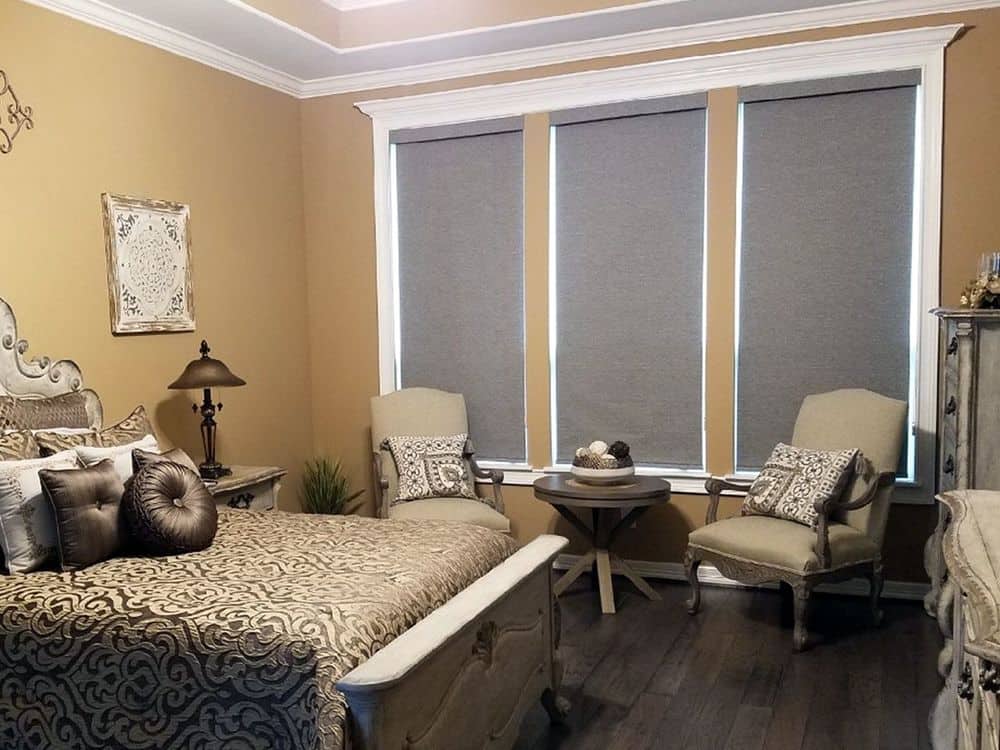 这间主卧室拥有一张豪华的床，旁边有一个休息区。这间房间的特色是硬木地板、棕色墙壁和托盘天花板。