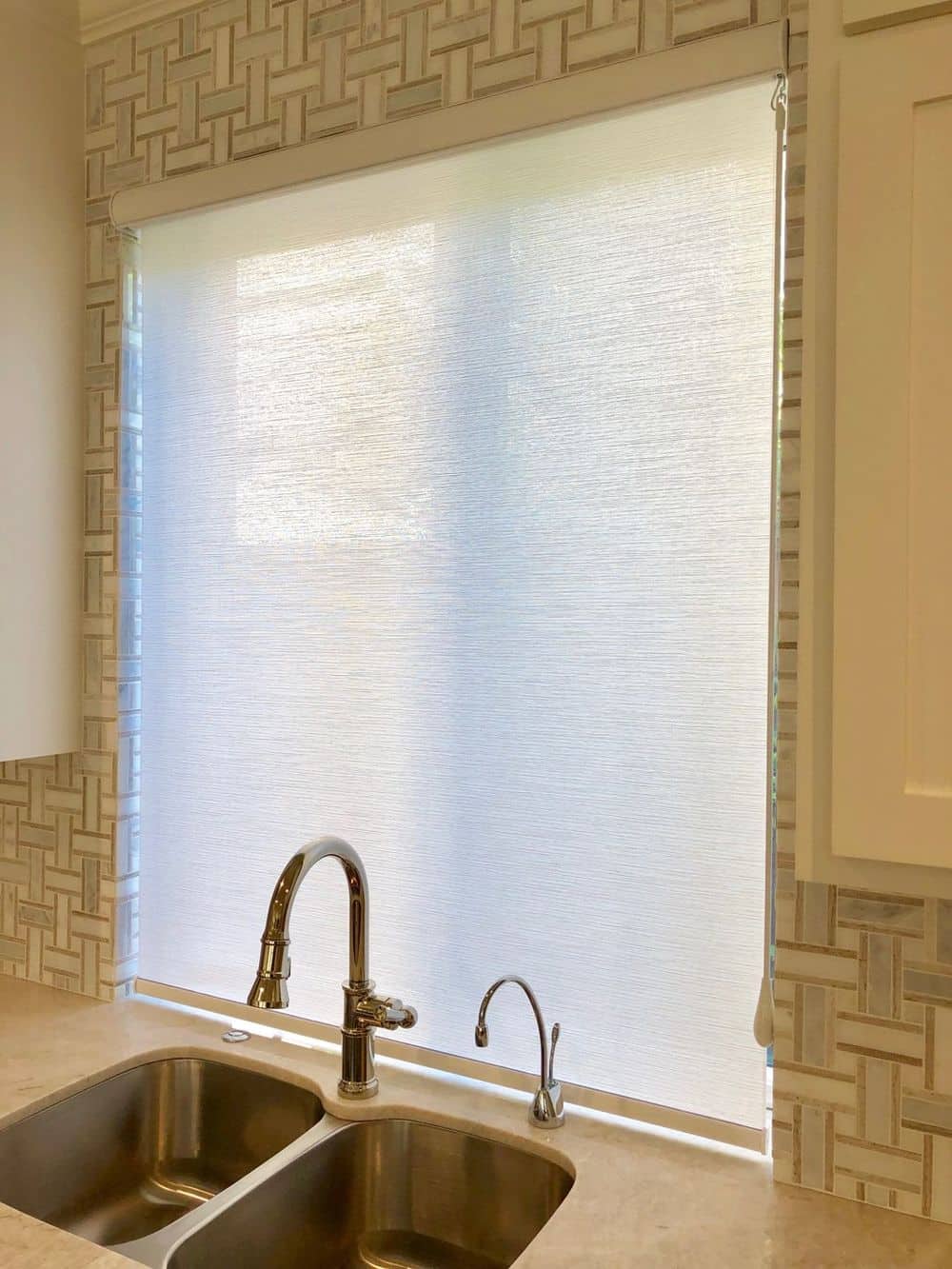 这张照片聚焦在这个家的厨房窗户上，窗户上有遮阳板。厨房的时尚水槽后挡板也可以看到。