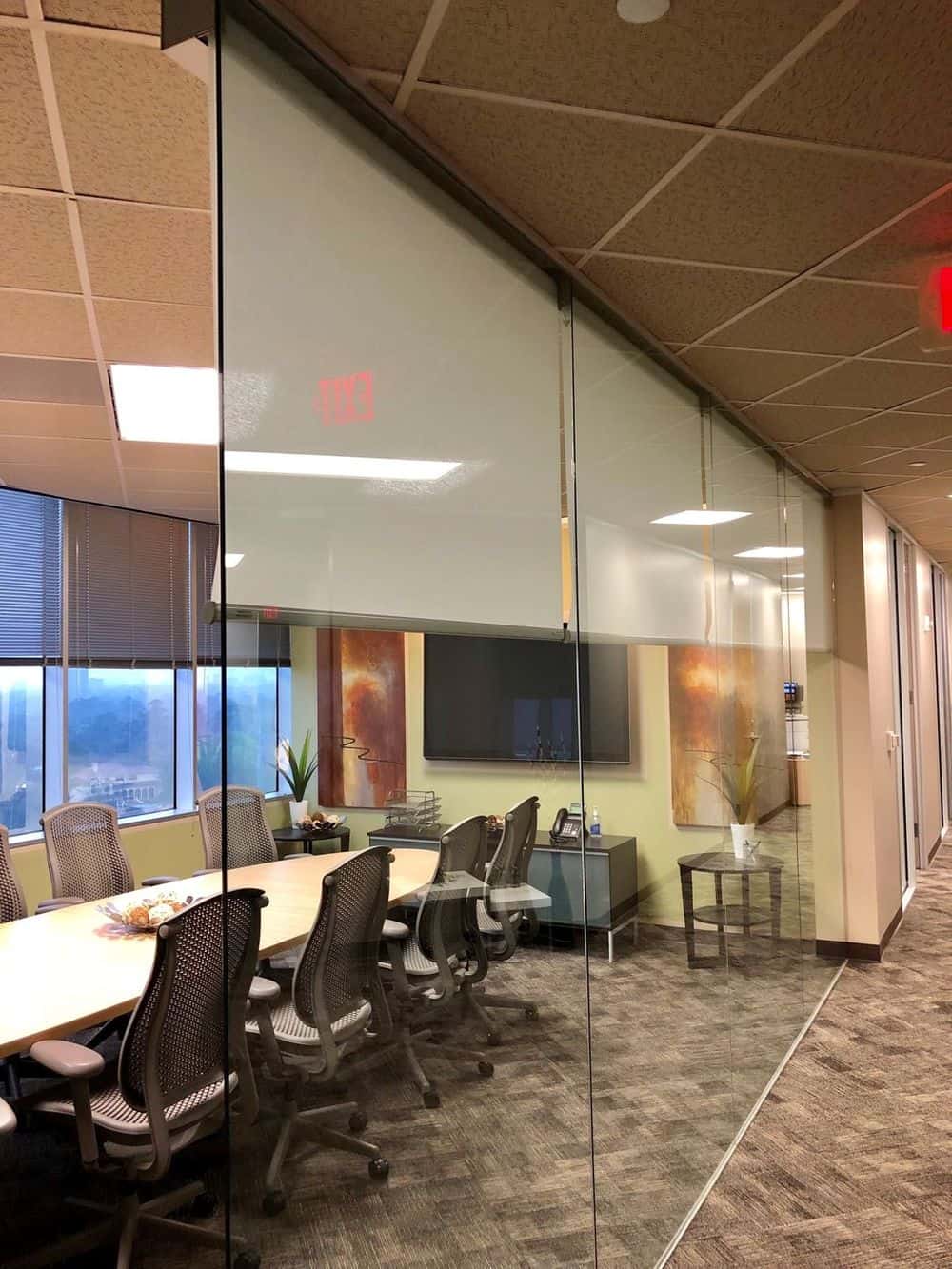 办公室会议室设有大玻璃墙，定制瓷砖天花板和时尚的地毯地板。房间里有一张长方形的长桌，配有现代化的办公椅，墙上有一台宽屏电视。
