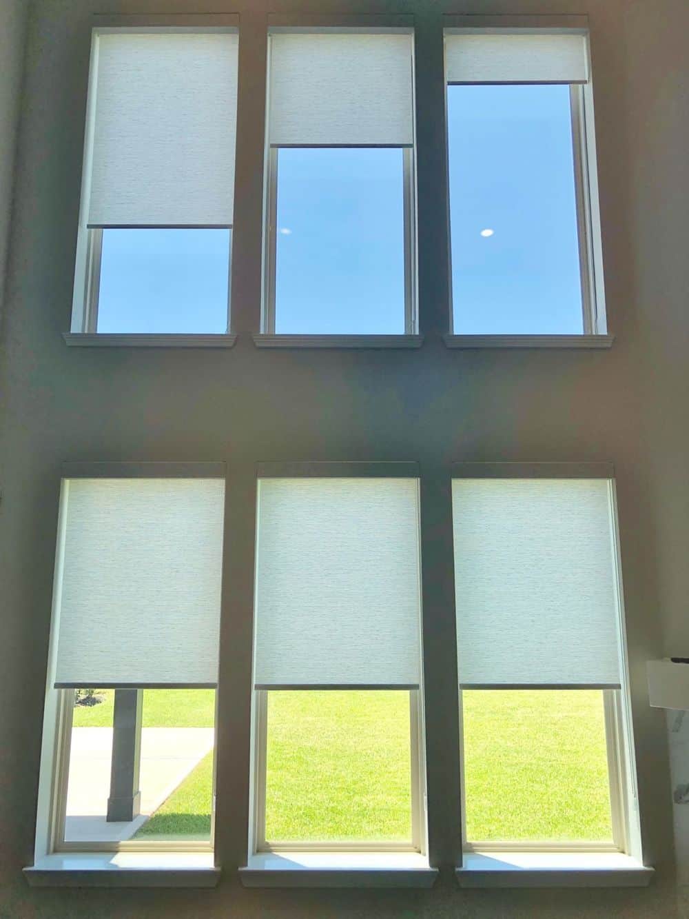 这张照片聚焦在这所房子的窗户上，以窗帘为特色。这座房子的特点是灰色的墙壁和高高的天花板。