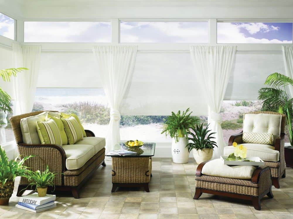 一个可爱的生活空间，提供一组漂亮的座位，以及带有白色窗帘和白色窗帘的大玻璃窗。