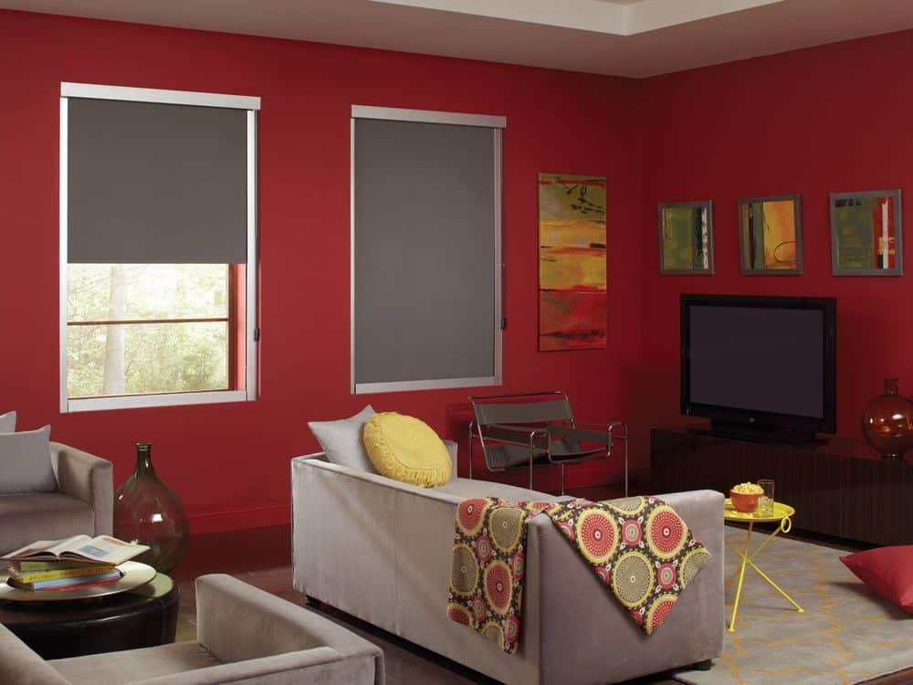 生活空间拥有一组现代灰色座椅，周围环绕着红墙、硬木地板和白色托盘天花板。房间里有几扇带遮阳帘的窗户，还有多处墙面装饰。