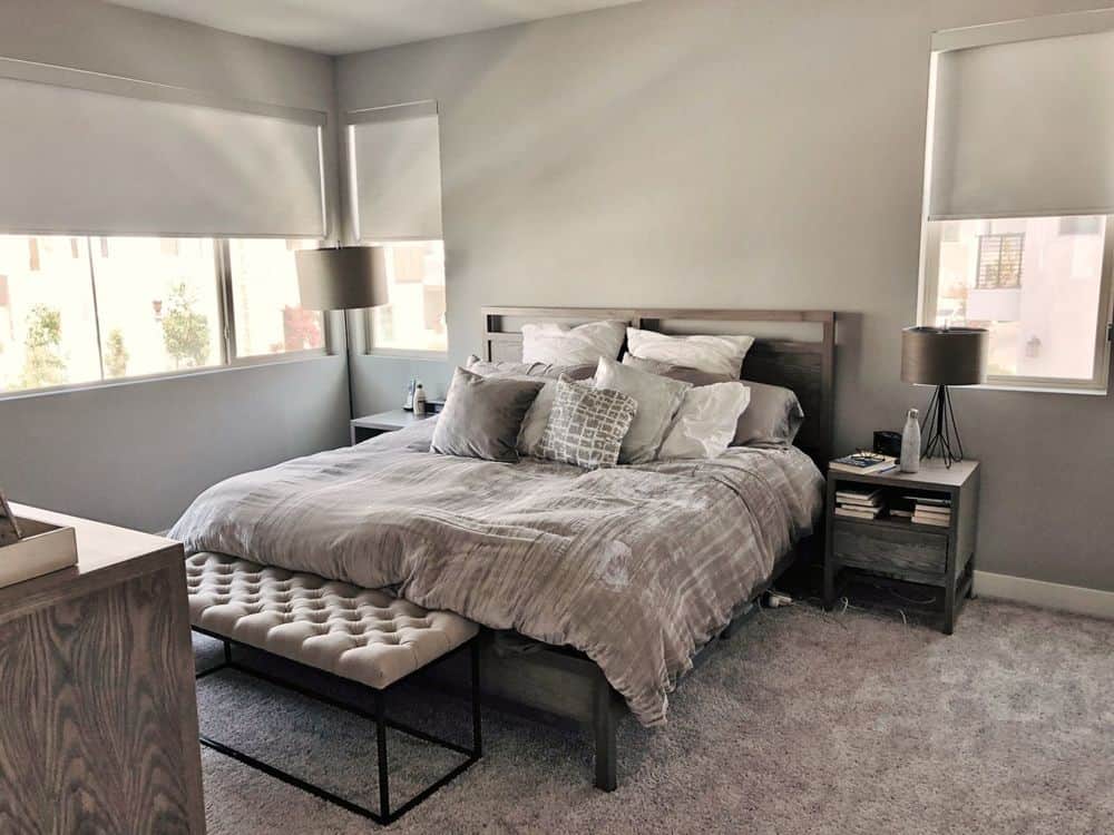 主卧室采用灰色地毯地板和灰色墙壁。它提供了一个舒适的床和两个边桌。窗户还设有卷帘窗帘。