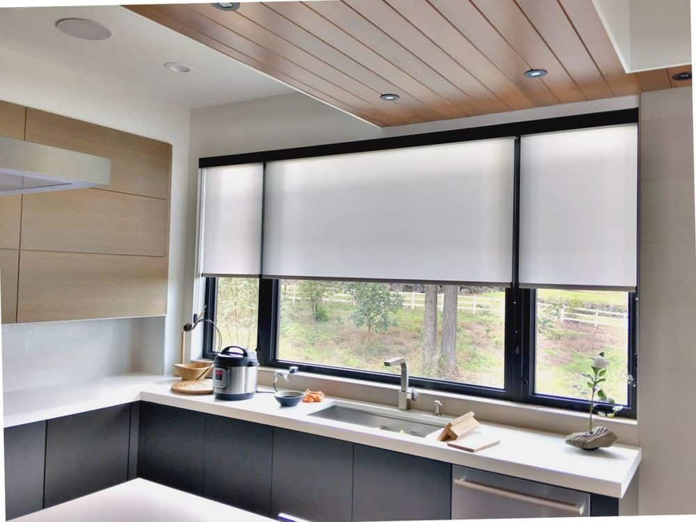 该厨房区域设有l型水槽柜台，定制天花板和带卷帘的玻璃窗。