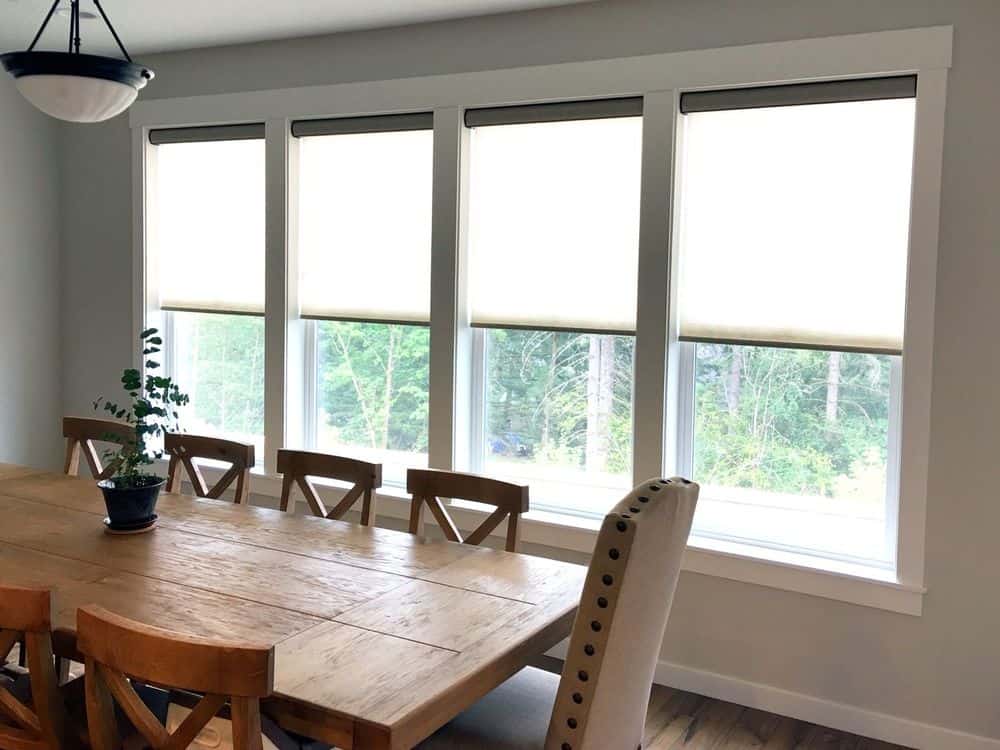 餐厅区设有木制矩形餐桌和椅子，周围环绕着浅灰色的墙壁和玻璃窗户，设有卷帘窗帘。