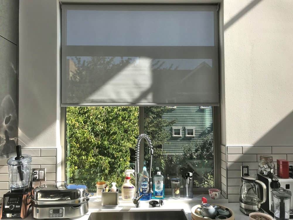 仔细看这个厨房的玻璃窗户，上面有灰色的卷帘。这间厨房还设有瓷砖后挡板和白色厨房台面。