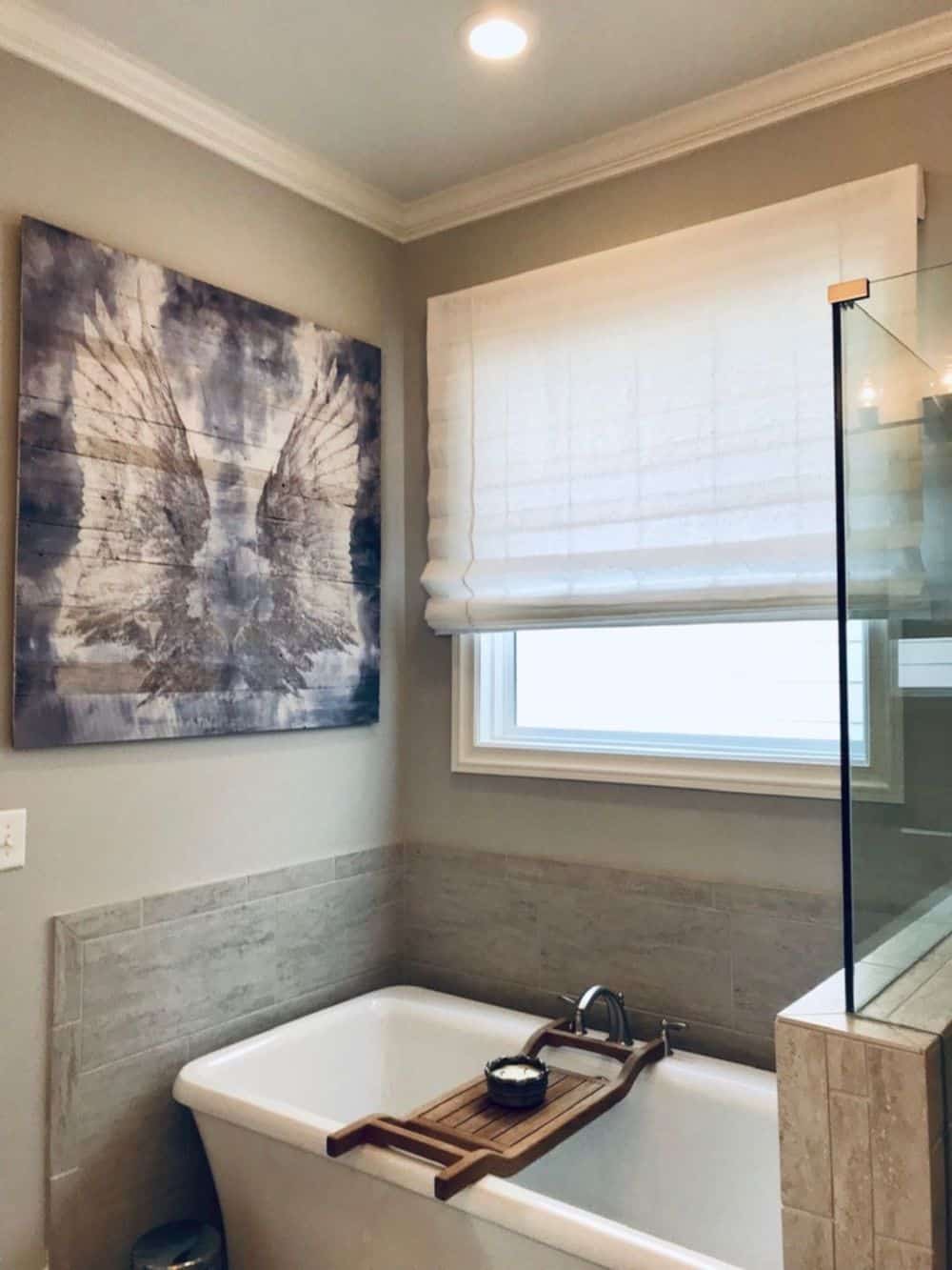主浴室设有步入式淋浴间和独立浴缸，靠近窗户，带有罗马风格的窗帘。墙上的装饰看起来很吸引人。