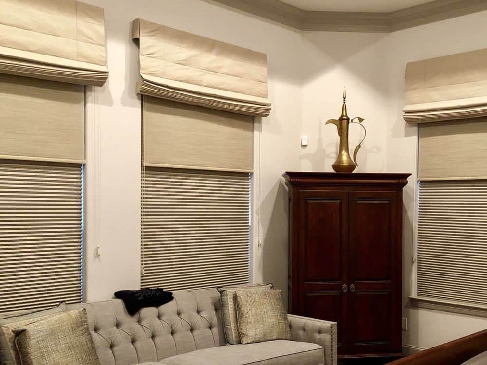 一个以带有罗马风格窗帘的窗户为特色的生活空间。房间提供舒适的沙发套装和角落里的橱柜。
