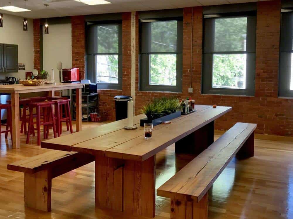 一个宽敞的餐厅拥有一个木制餐桌和长凳座椅设置硬木地板和砖墙。房间也有带有太阳能窗帘的窗户。