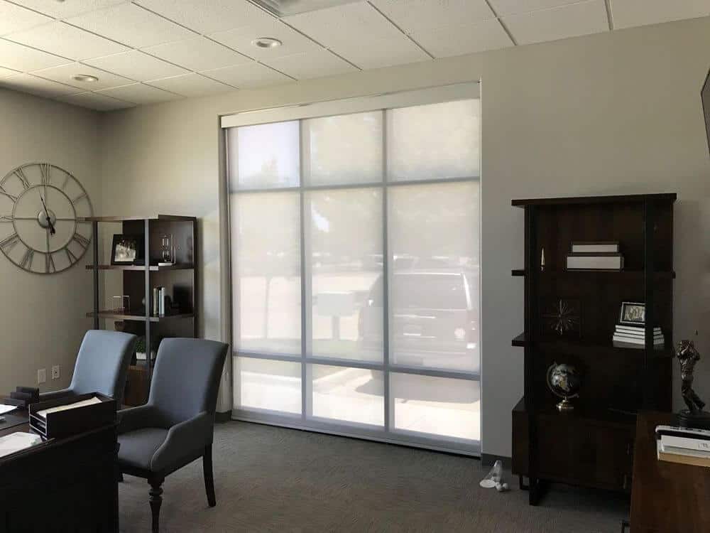 宽敞的家庭办公室设有浅灰色的墙壁，地毯地板和带有嵌入式顶灯的瓷砖天花板。房间提供桌子和现代椅子，以及独立的架子。