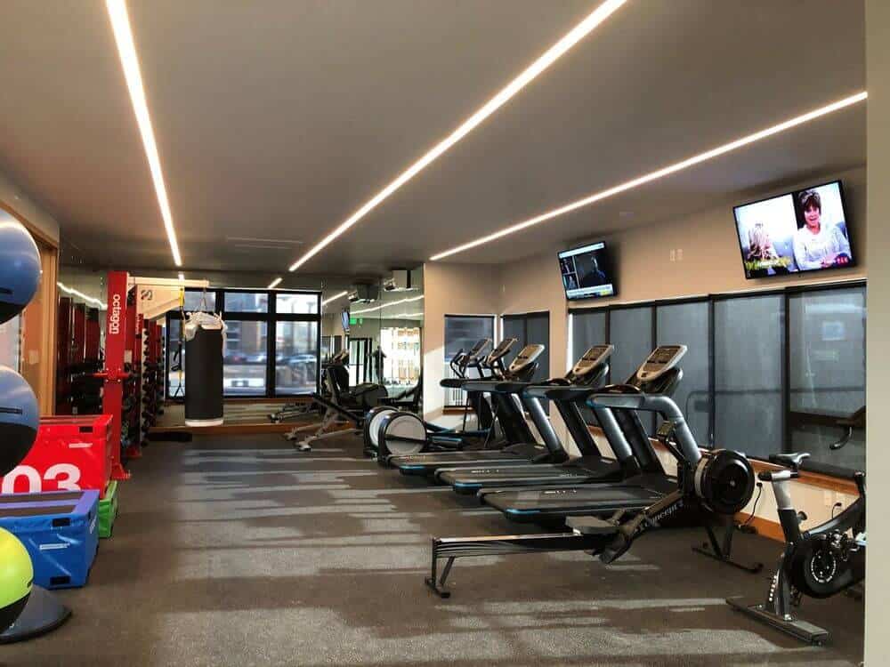 宽敞的健身房拥有维护良好的机器和其他设备，以及墙上的两台电视和时尚的天花板照明，以及地毯地板。