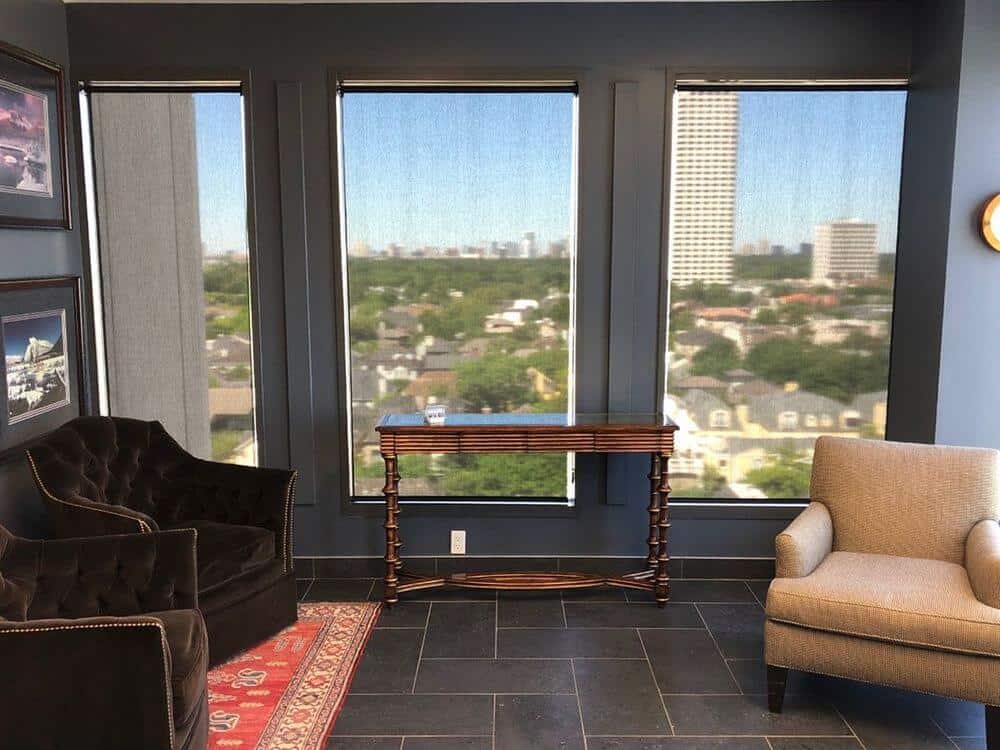 一个生活空间设有优雅舒适的座椅和瓷砖地板，上面有一个区域地毯。房间的特点是灰色的墙壁和玻璃窗。