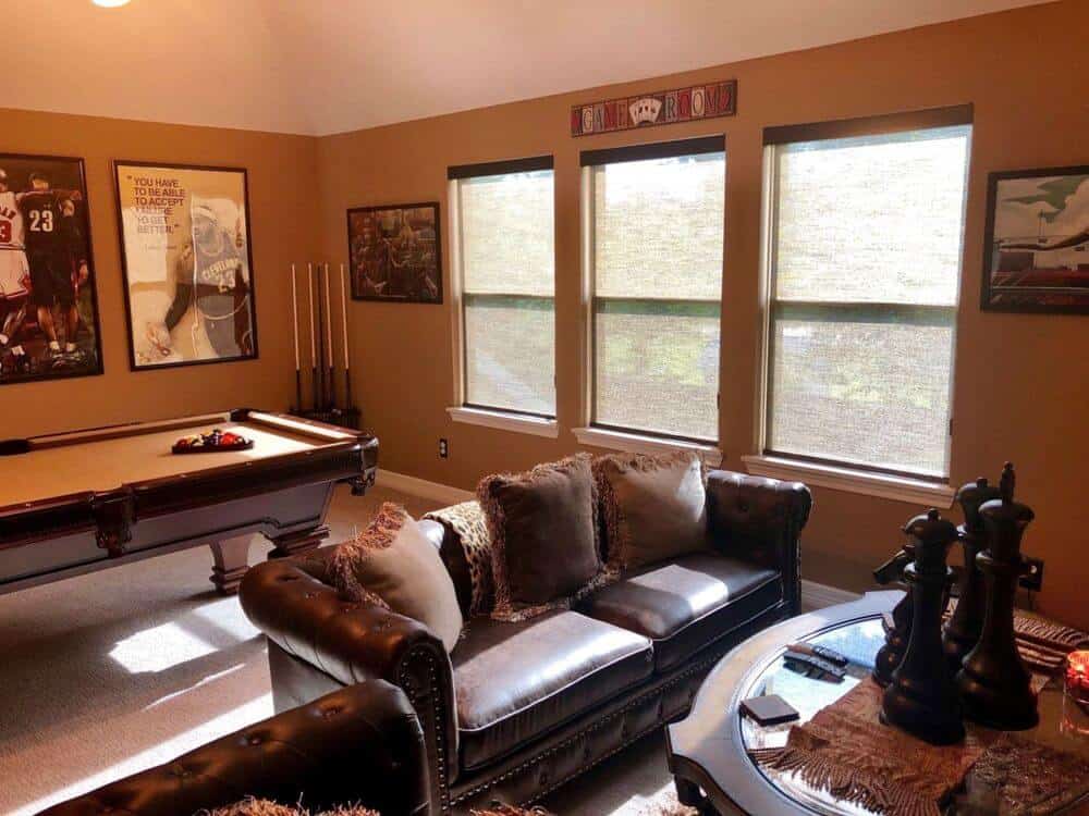一个游戏室拥有一个皮革沙发套和一个中心桌，以及一个台球桌在一侧。房间的特色是棕色的墙壁和地毯地板。