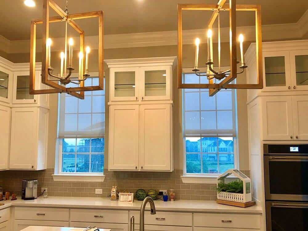 这个厨房的特色是白色的厨房柜台和白色的橱柜，以及一个由迷人的吊灯照亮的白色小桌。