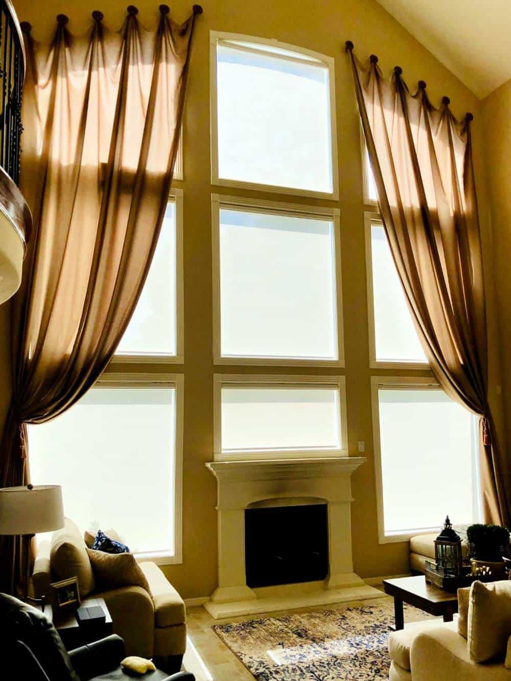 这间客厅配有一套优雅的沙发和壁炉，位于住宅的高高的天花板下。该区域的窗户以优雅的窗帘和太阳能窗帘为特色。