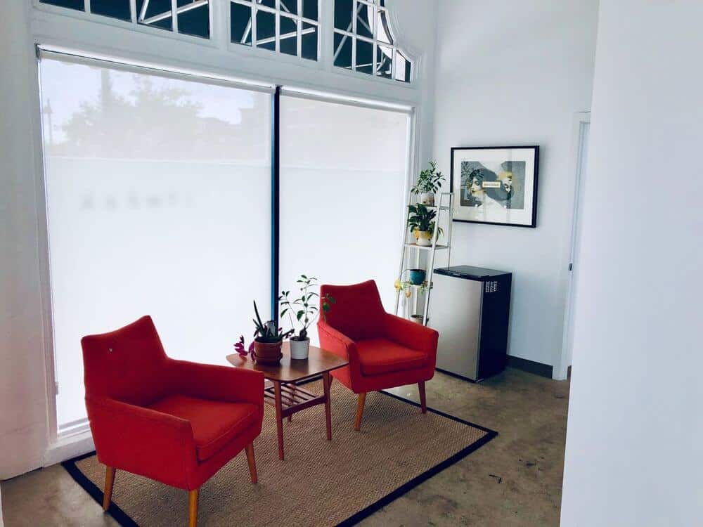 休息区有一对可爱的红色座椅，中间的桌子放在小地毯上，周围是白色的墙壁和高高的天花板。