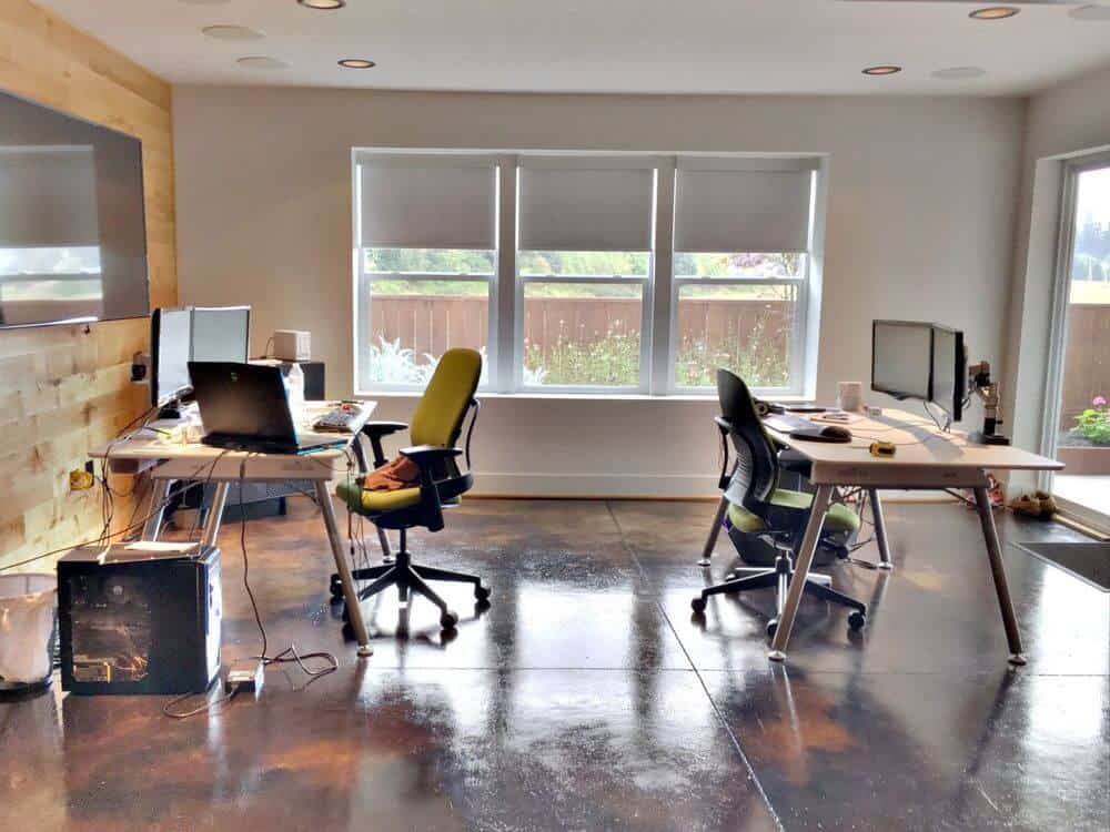 办公区域以时尚的瓷砖地板和浅灰色的墙壁以及木墙为特色。这里有两张办公桌，配上现代风格的椅子，还有带嵌壁灯的普通天花板和带遮阳板的玻璃窗。