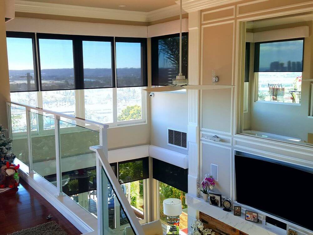 大型现代住宅，在住宅的高天花板下的起居空间的墙上有一个巨大的平板电视，周围环绕着带有太阳能窗帘的玻璃窗。