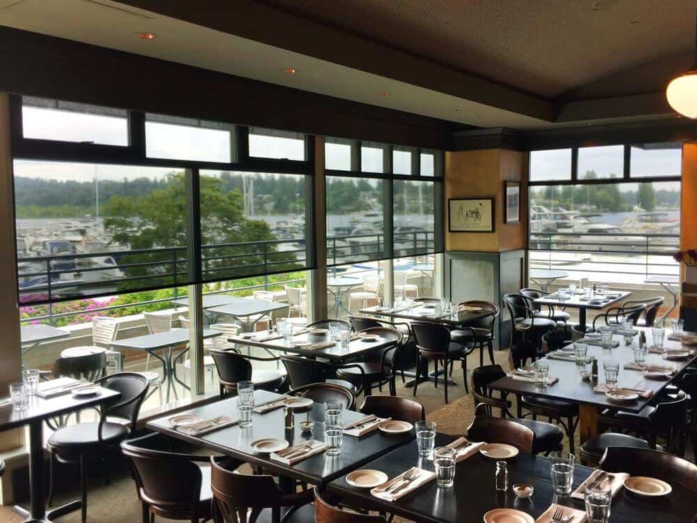 餐厅的用餐区，有几张桌子，有灰色的托盘天花板和大玻璃窗。