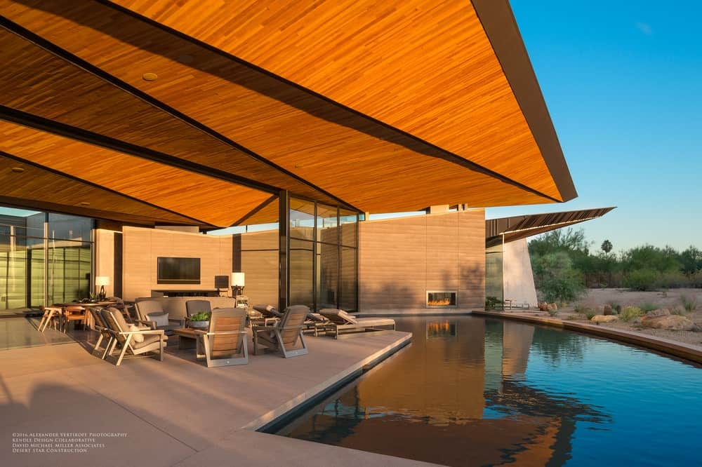 混凝土、金属和玻璃为这个室外生活区的有机形式提供了平衡，该生活区具有超大的木质天花板、座位区和带壁炉墙的定制游泳池。
