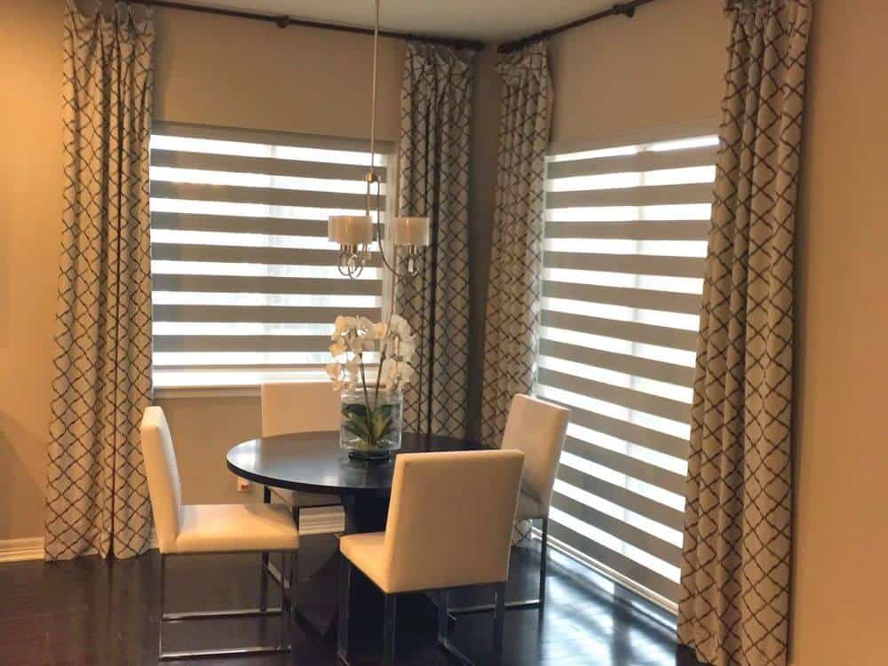 用餐区设有一个圆形餐桌，由小吊灯照明的现代椅子。房子的特点是有过渡窗帘的窗户。