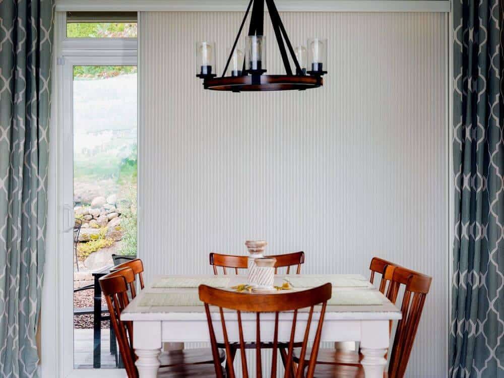 专注地看这个家的优雅的餐桌和椅子设置由华丽的天花板灯照亮。窗户被垂直的蜂窝窗帘覆盖。