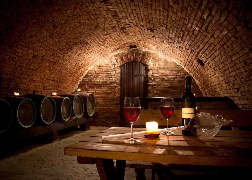 一个大型地下酒窖，设有木制桌椅，砖墙和天花板。