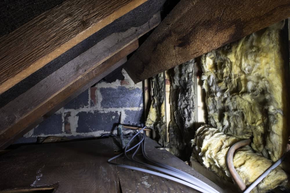 房子屋檐下的爬行空间展示了旧的玻璃纤维绝缘、管道、椽子、风块结构和旧木板。