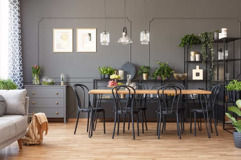 灰色餐厅，有护壁墙，硬木地板，木制餐桌周围是黑色圆形靠背椅，金属架子，玻璃挂件，艺术品和小盆栽。