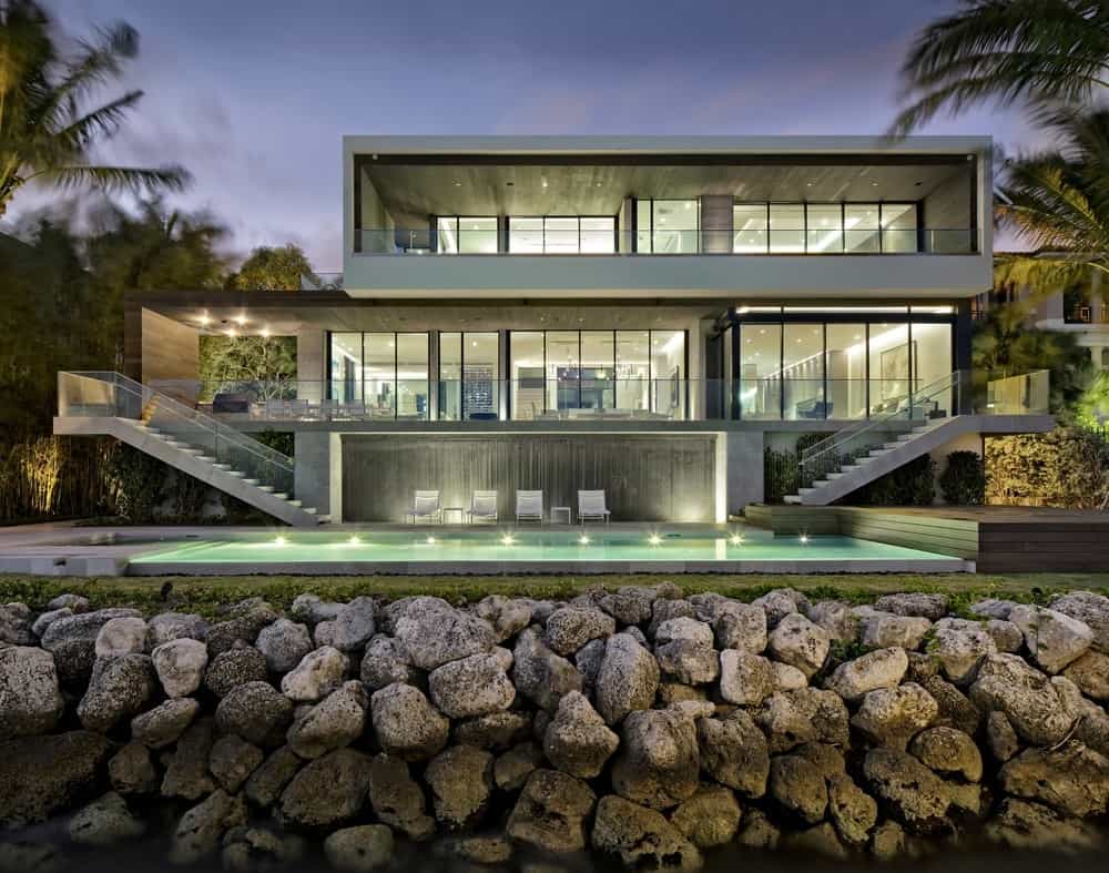 一座现代住宅拥有简约的设计，坐落在石头挡土墙上。它有宽敞的阳台和两端的混凝土楼梯，通往宁静的游泳池。