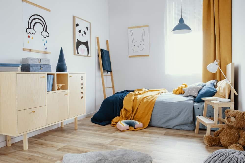 儿童卧室，宽木板地板，白墙，轻木梳妆台，舒适的床，吊灯，梯子和可爱的海报。
