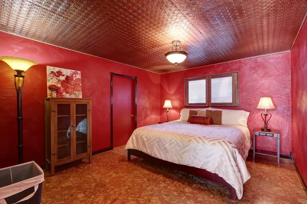 红色主卧室，装饰瓷砖天花板，棕色地板，红色纹理墙壁，木制家具和环境照明。