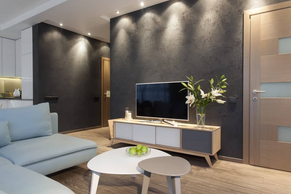 小客厅，宽木板地板，灰色纹理的墙壁，凹形灯，l形沙发，模块化咖啡桌和一个轻木架上的平板电视。