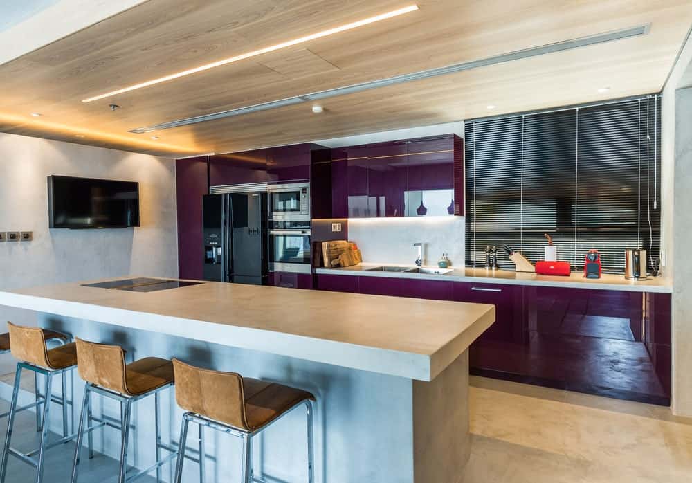 这是一个有着时尚和现代外观的厨房，深紫色的橱柜使黑色的电器脱颖而出。这与一个大厨房岛台搭配，与天花板的色调相匹配。