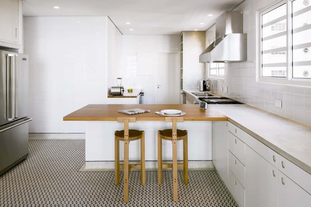 这是一个明亮的厨房，白色的橱柜和厨房半岛上的木制台面，搭配一对木制凳子作为早餐吧。