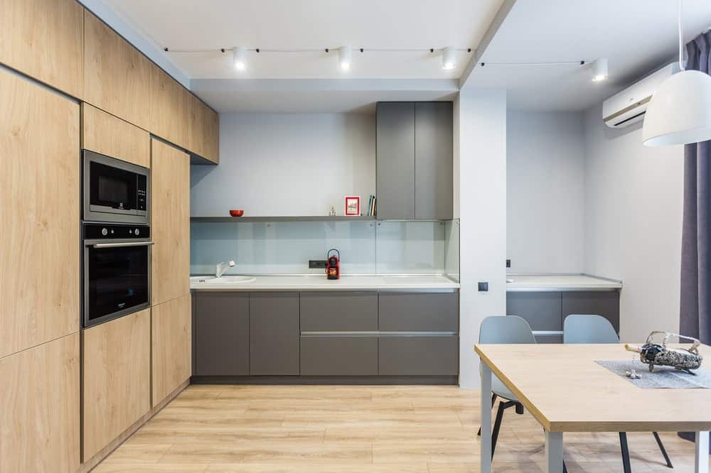 这是现代厨房的一个视图，在一侧有一个大的木结构，与地板相匹配，与厨房的灰色橱柜相辅相成。
