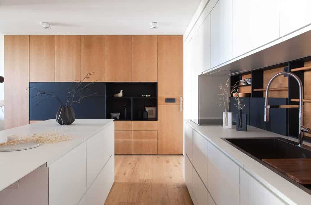 这个厨房有一个现代的设计，展示了全高的木制橱柜，中间有黑色的架子，白色的岛与面对的橱柜和柜台相匹配。