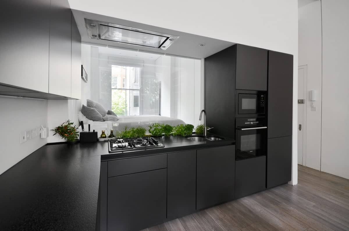 光滑的厨房，对比鲜明的白色和木炭橱柜，配有黑色电器。它的特点是镜子的后挡板，卧室被反射。