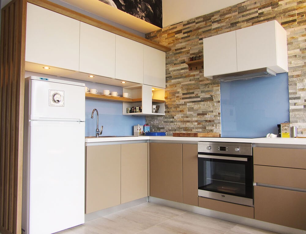 这间厨房的砖砌后挡板与极简主义的白色和灰褐色橱柜增添了质感。它配备了一个炉子、白色冰箱和一个装有鹅颈龙头的下置水槽。