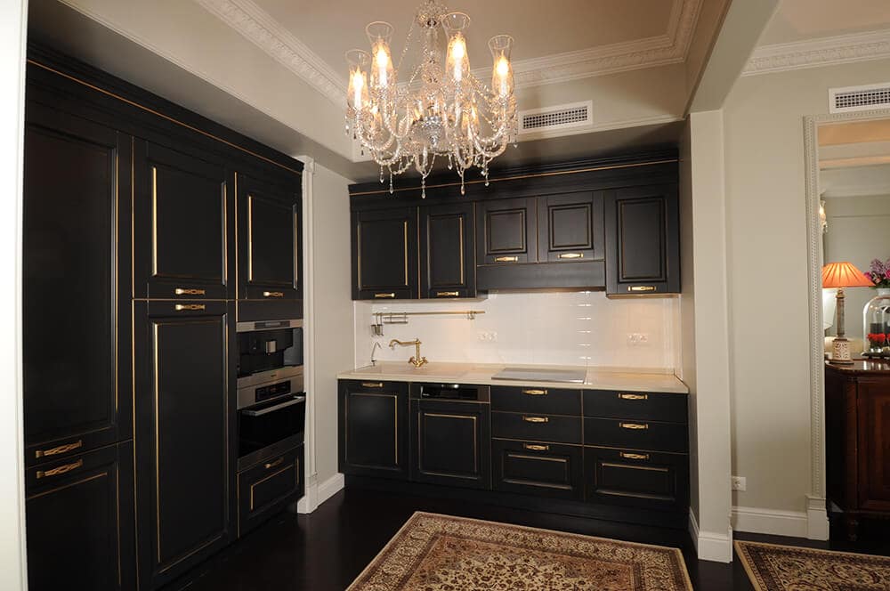 优雅的厨房，经典的地毯上悬挂着一盏串珠吊灯。它具有哑光黑色橱柜与黄金五金和装饰强调。