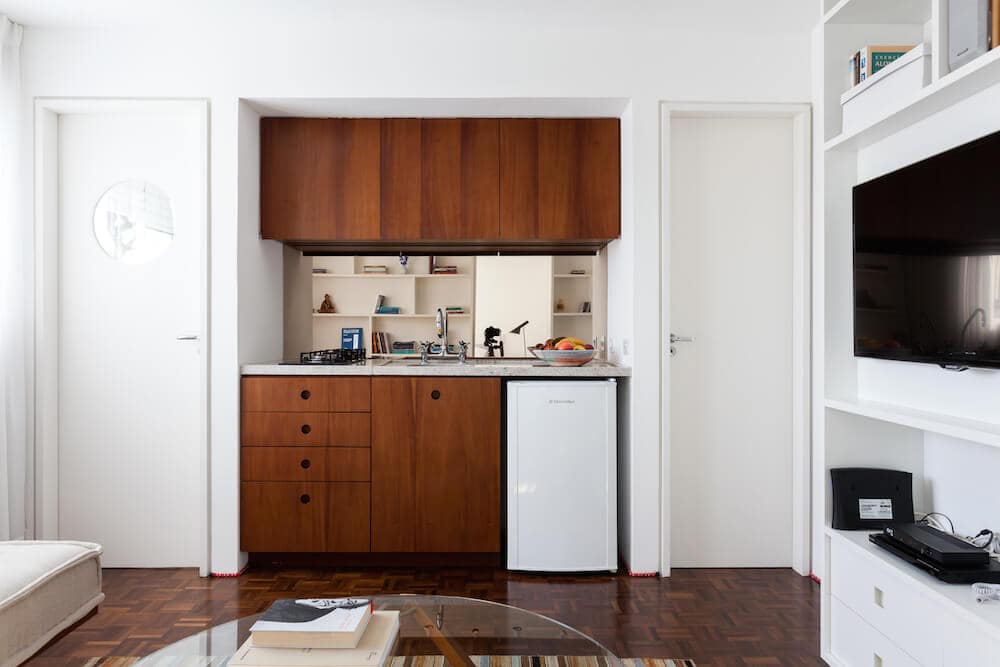 小厨房两侧是一模一样的白色门，由丰富的木质橱柜和花岗岩台面组成。它包括一个白色的小冰箱和一个装有镀铬装置的水槽。