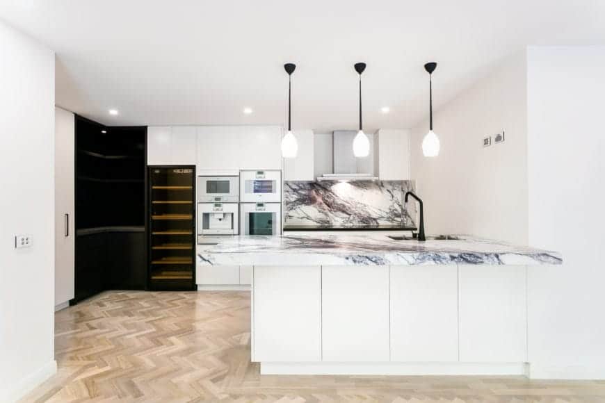 现代厨房拥有白色的墙壁和橱柜，与黑色的角架和葡萄酒冰箱形成对比。大理石台面和后挡板为该地区增添了豪华的感觉。